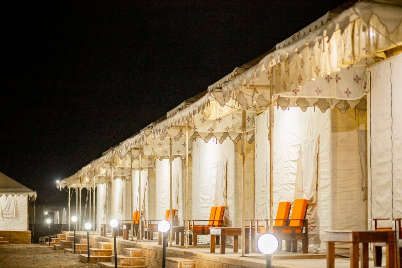 Une rangée de tentes, chacune équipée d’un espace pour s’asseoir et d’une source de lumière placée au sol.