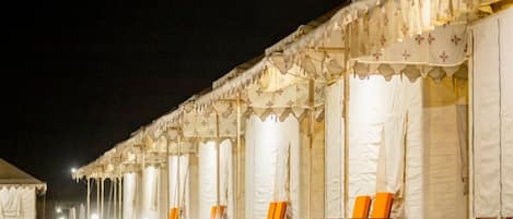 A row of tents with seating areas, each with a light source on the ground.