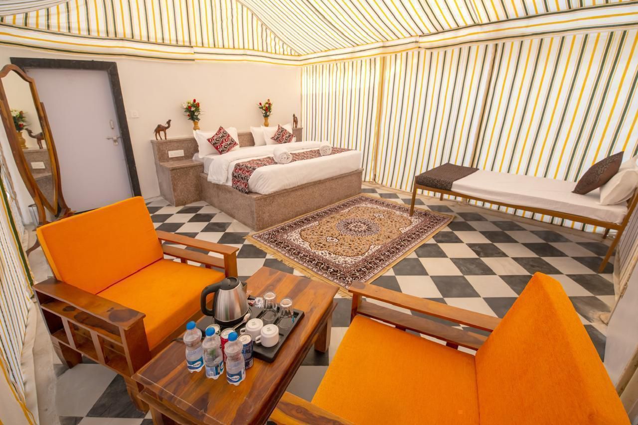 A hotel room with a checkered floor, a bed with patterned bedding, a sofa, a dining table with a tray of items, and a mirror.