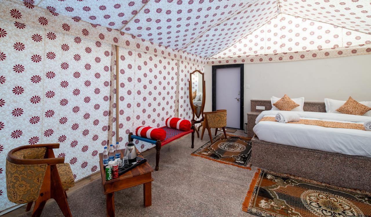 A room with a bed, a chair, a table with bottles, and a mirror.