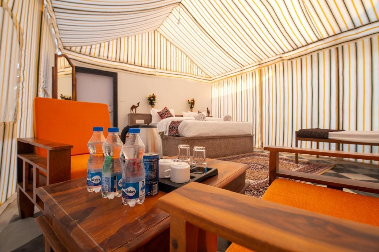 A tent-style room with a bed, seating area, and a table with water bottles and cups.