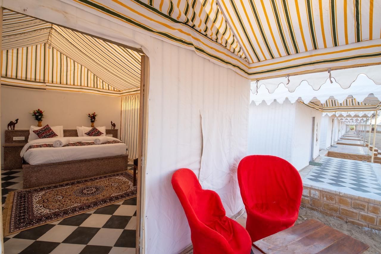 A room with a bed, a red chair, a patterned rug, and a checkered floor.