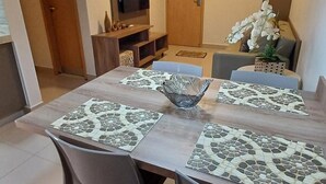 A dining area with a wooden table, two chairs, a central glass bowl, and a television in the background. - Park Veredas Resort (Rio Quente)