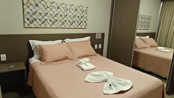 Quarto de hotel com cama, mesa de cabeceira, espelho e um ornamento geométrico na parede.