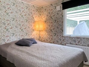 A bedroom with a bed, a wall-mounted lamp, and a window with a view of greenery. - 6 Person Holiday Home in Gunnebo (Gunnebo)