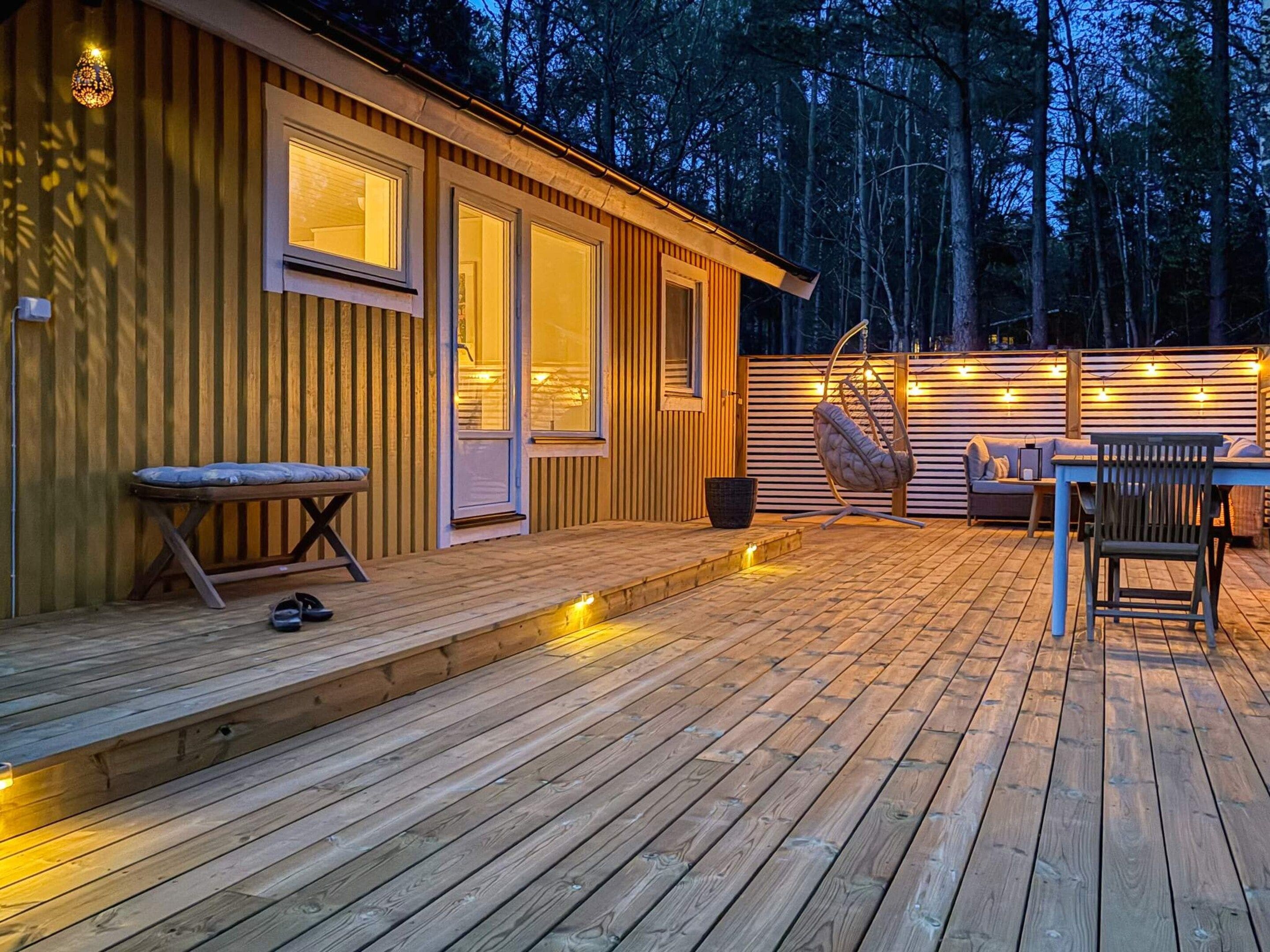 Une terrasse en bois avec un banc, un fauteuil suspendu et une table.