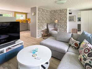 A modern living room with a flat-screen TV, a sofa, a coffee table, and a patterned wallpaper. - 6 Person Holiday Home in Gunnebo (Gunnebo)