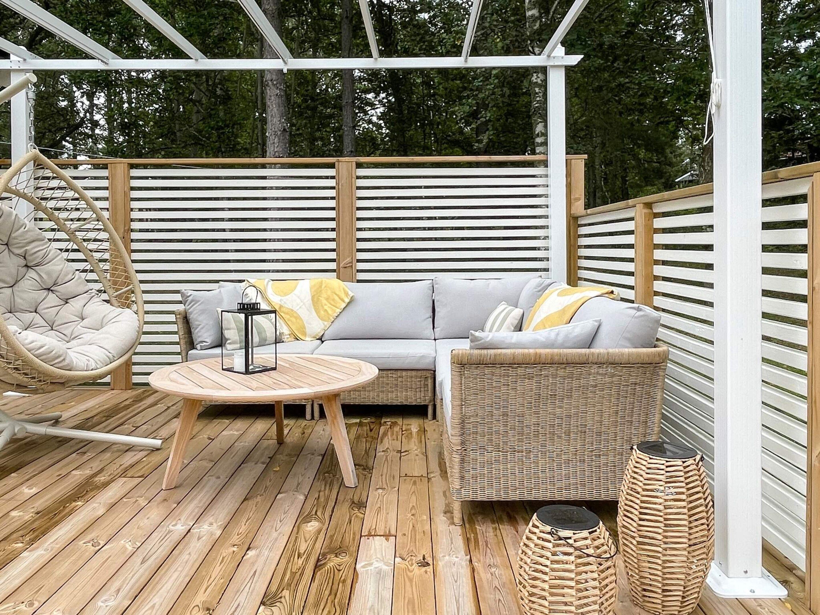 A wooden deck with a wicker sofa, a hanging chair, and a round table.