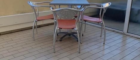 A balcony with a table and chairs, a tiled floor, and a view of houses and trees.