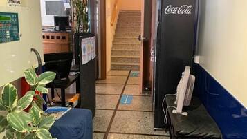 Un corridoio di un hotel con una scala, un frigorifero Coca-Cola, una scrivania con un computer e una pianta in vaso.