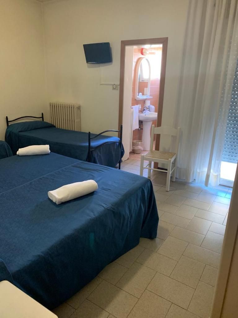Una camera d'albergo con due letti, una sedia, un termosifone e una TV a parete.
