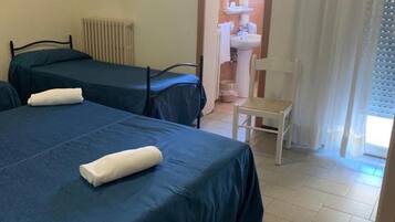Una camera d'albergo con due letti, una sedia, un termosifone e una TV a parete.