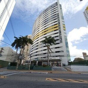 A multi-story hotel with a curved facade, palm trees in front, and a clear sky. - Natal Plaza Requinte Conforto E Vista Para O Mar (Natal)