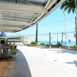 An outdoor area with a covered walkway, palm trees, and a view of the sea. - Natal Plaza Requinte Conforto E Vista Para O Mar (Natal)