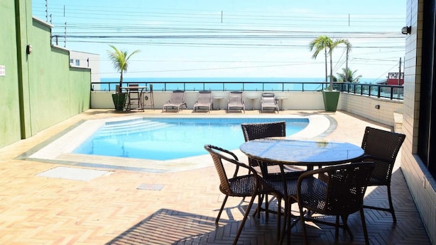 A rooftop pool area with a view of the ocean, equipped with lounge chairs and a table. - Natal Plaza Requinte Conforto E Vista Para O Mar (Natal)