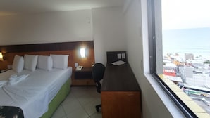 A hotel room with a bed, a desk, and a window with a view of the city and the sea. - Natal Plaza Requinte Conforto E Vista Para O Mar (Natal)