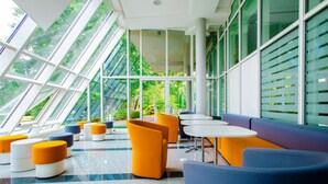 A modern interior with a checkered floor, seating areas with orange and blue furniture, and large windows offering views of greenery. - Genohotel (Karlsruhe)