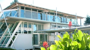 A modern building with a glass facade, a staircase, and a well-maintained garden with large green leaves and red flowers. - Genohotel (Karlsruhe)