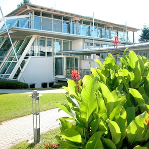 Ein modernes Gebäude mit Glasfassade, einer Treppe und einem gepflegten Garten mit großen grünen Blättern und roten Blüten.