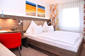 Ein Hotelzimmer mit Bett, Schreibtisch, Stuhl und einem fenster mit Vorhängen.