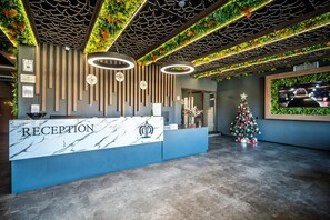 A reception area with a marble counter, vertical wooden slats on the wall, circular ceiling lights, and a Christmas tree. - Hotel Royal Bath (Karlovo)