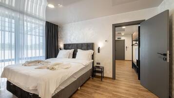 Habitación de hotel moderna con una cama grande, una mesita de noche, un armario y vistas a través de una ventana con cortinas traslúcidas.