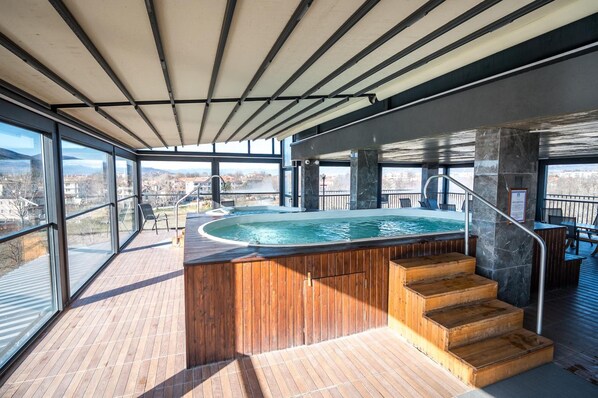 A modern indoor swimming pool with a wooden deck and a view of the city. - Hotel Royal Bath (Karlovo)