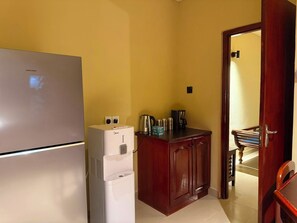 Une cuisine compacte équipée d’un réfrigérateur, d’un distributeur d’eau et d’une machine à café, le tout installé sur un comptoir en bois.