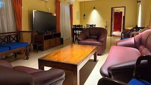 Ein Hotelzimmer mit einem Holztisch, Ledersofas, einem Flachbildfernseher und einem Essbereich mit Stühlen.