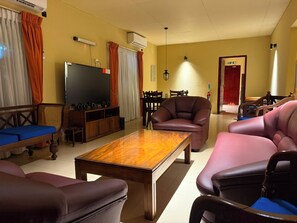 A hotel room with a wooden coffee table, leather sofas, a flat-screen TV, and a dining area with chairs. - Don Cyril's Nature Bungalow (Galle)