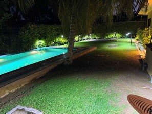 Une piscine entourée d’une pelouse et de palmiers, le tout éclairé par un système d’éclairage d’ambiance.