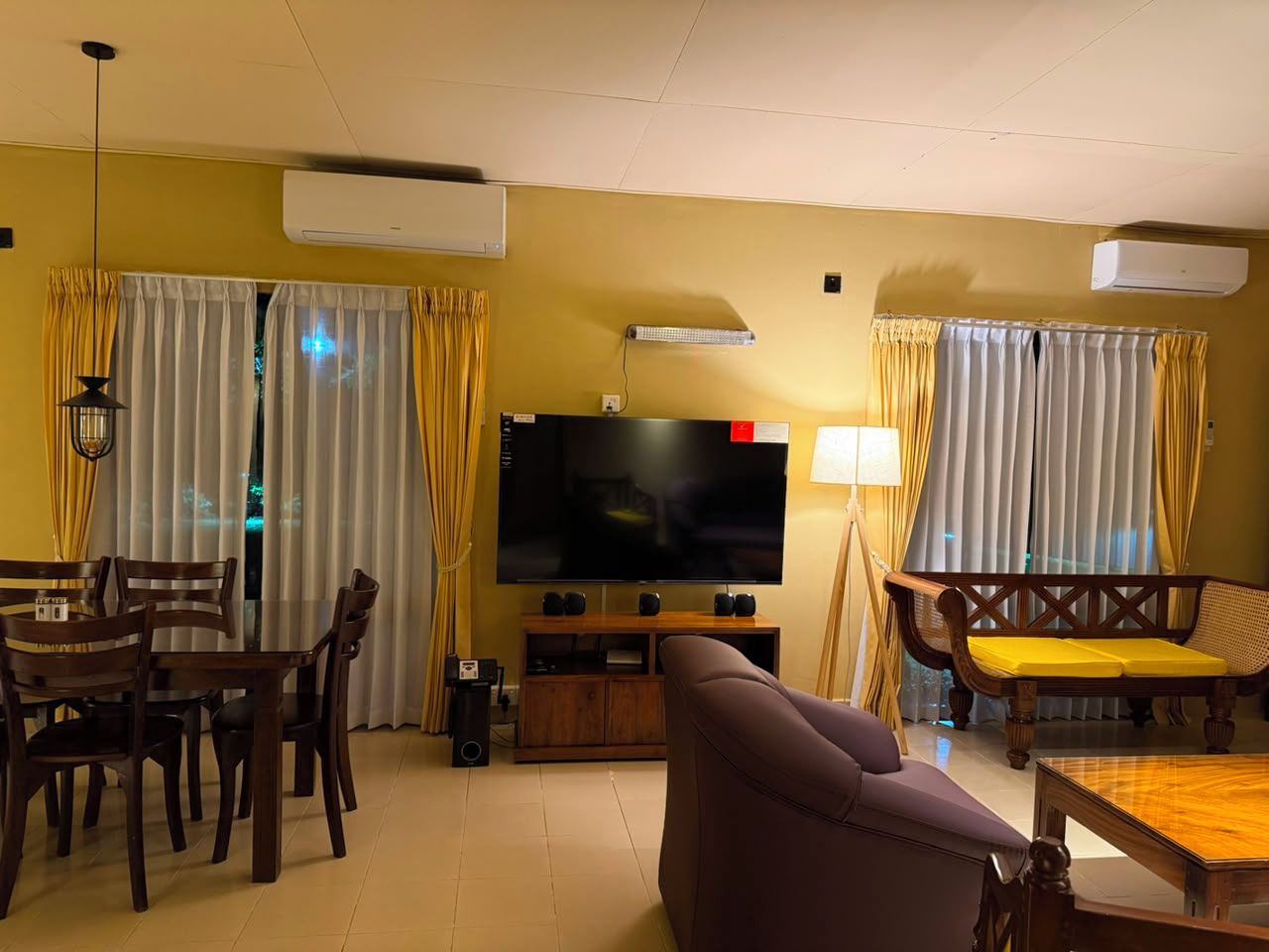Una sala de estar con televisor de pantalla plana, muebles de madera y cortinas amarillas.