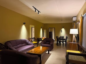 A living room with a sofa, armchair, coffee table, and a dining area with chairs and a table. - Don Cyril's Nature Bungalow (Galle)