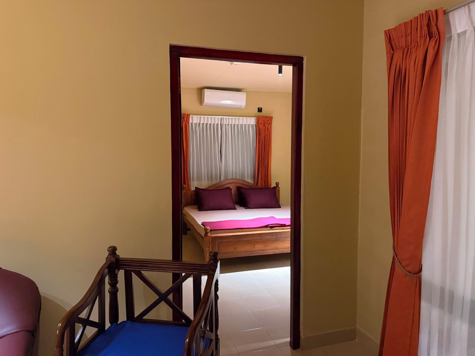 Un dormitorio con cama, una silla de madera y un espejo que refleja la habitación.
