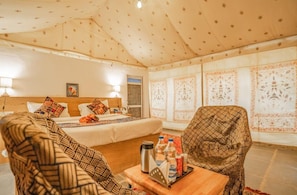 Ett hotellrum med en säng, en soffa, en stol, ett brickbord med drycker och ett mönstrat tak.