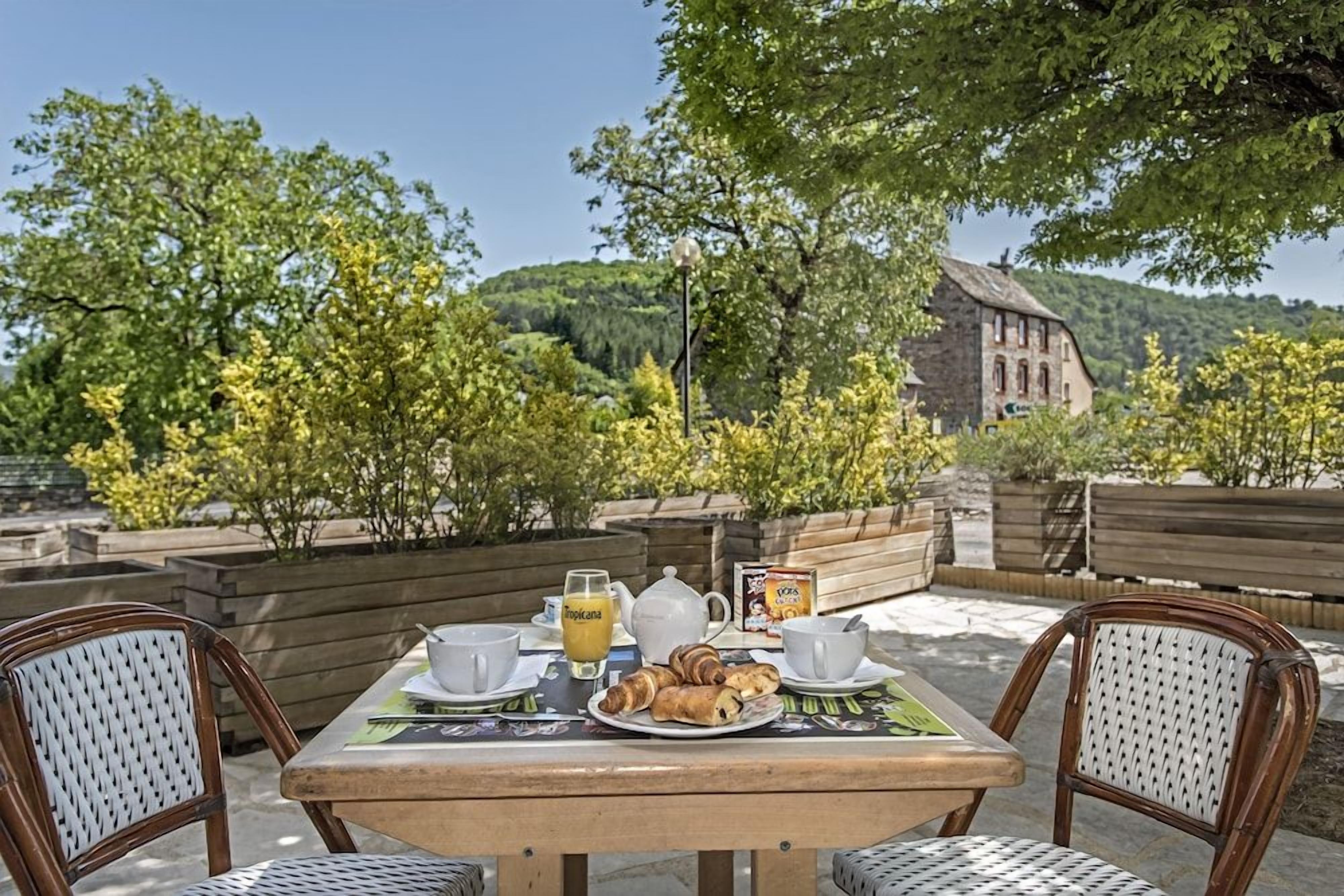 An outdoor dining area with a table set for two, featuring a plate of croissants, a teapot, cups, and a glass of orange juice.
