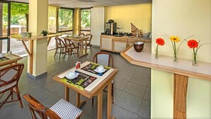 A dining area with tables and chairs, a counter with a cash register, and a wall with flower arrangements. - Hotel Eco - A75 (Banassac)