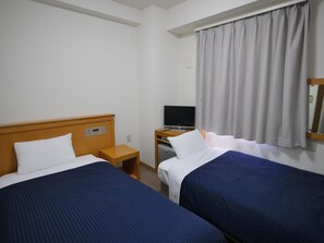 Une chambre d’hôtel avec deux lits, une télévision, une petite table et une fenêtre avec des rideaux.