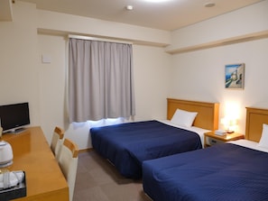 Una camera d'albergo con due letti, una scrivania con un computer, una sedia, una finestra con tende e un quadro appeso al muro.
