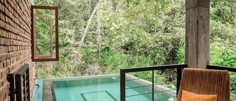 Área da piscina com uma cadeira e vista para o verde ao redor.