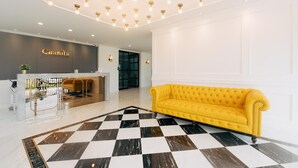 Un vestíbulo de hotel con suelo a cuadros, un mostrador de recepción, un sofá amarillo e iluminación empotrada en el techo.