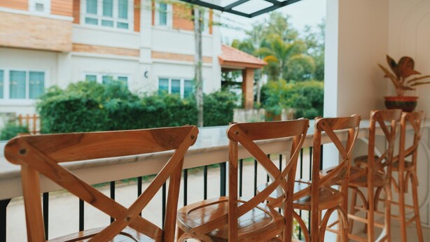 Una silla de madera con estructura metálica, ubicada en un balcón con vistas a un edificio y zonas verdes.