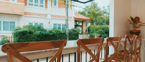 A wooden chair with a metal frame, positioned on a balcony with a view of a building and greenery.