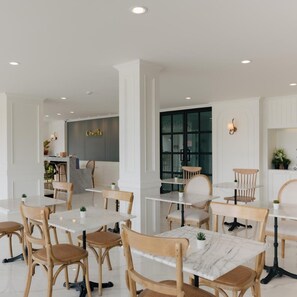 A modern restaurant interior with marble tables and wooden chairs, a visible sign reading 'Chantilly', and a large window allowing natural light. - Chanita Hotel Chumphon (Chumphon)