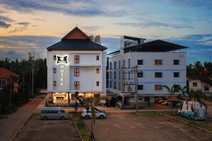 A hotel with a prominent sign, multiple floors, and a parking area with vehicles. - Chanita Hotel Chumphon (Chumphon)