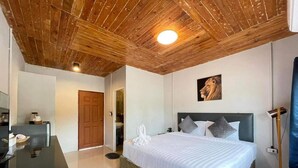 Quarto com teto de madeira, cama com almofadas, pintura na parede e escrivaninha com abajur.