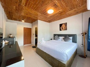 A bedroom with a wooden ceiling, a bed with pillows, a painting on the wall, and a desk with a lamp. - Mook Boonchu Hotel (Ko Mook)