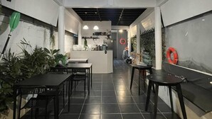 Interior de restaurante com balcão central, piso ladrilhado preto e plantas em vasos.