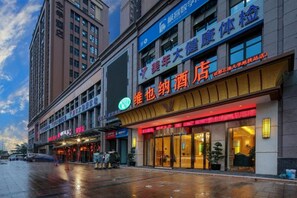 Un hotel con un letrero llamativo, varias tiendas y una calle mojada.