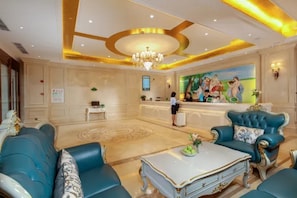 A hotel lobby with a reception desk, seating area with sofas, a chandelier, and a mural on the wall. - Vienna Hotel (Chengdu)
